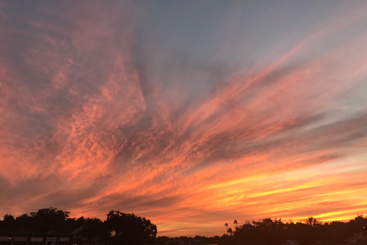 Sunset with pink and orange clouds over a calm river and tree silhouettes.