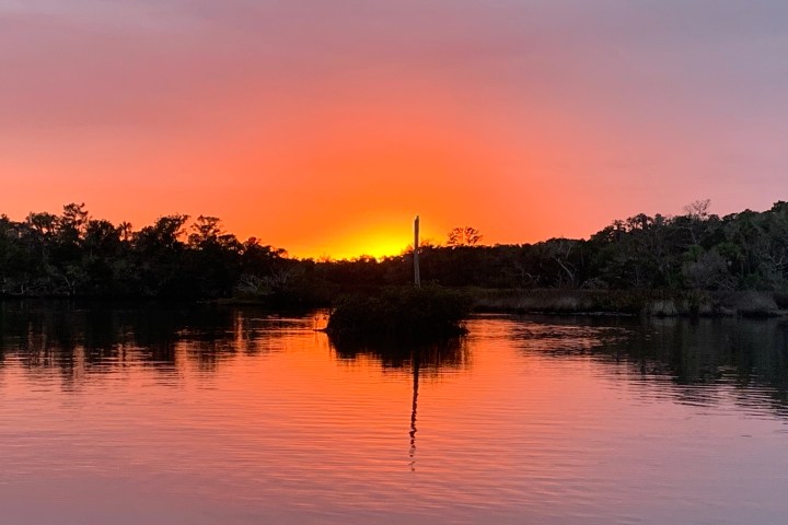 Sunset over a lake with silhouetted trees and pink-orange sky.