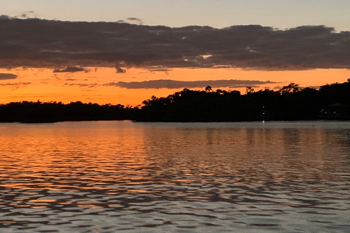 Sunset over a calm lake with silhouetted trees and orange sky.