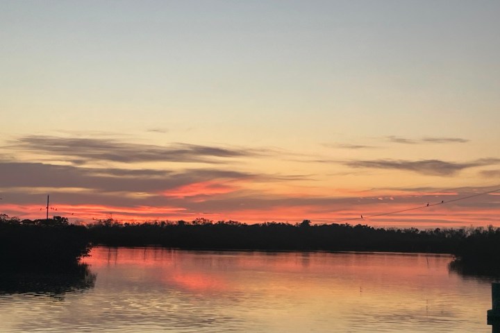 Sunset over a calm lake with silhouetted trees and pink-orange sky.