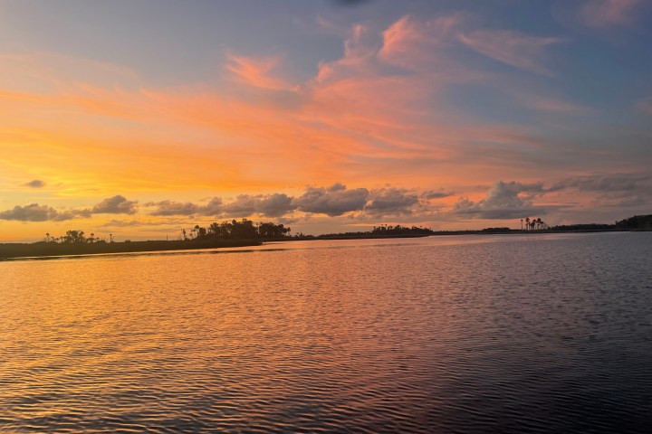 Serene lake at sunset with orange sky and distant trees.
