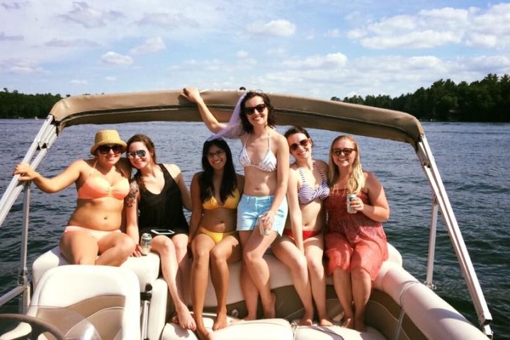 Six people on a boat smiling under a sunny sky.