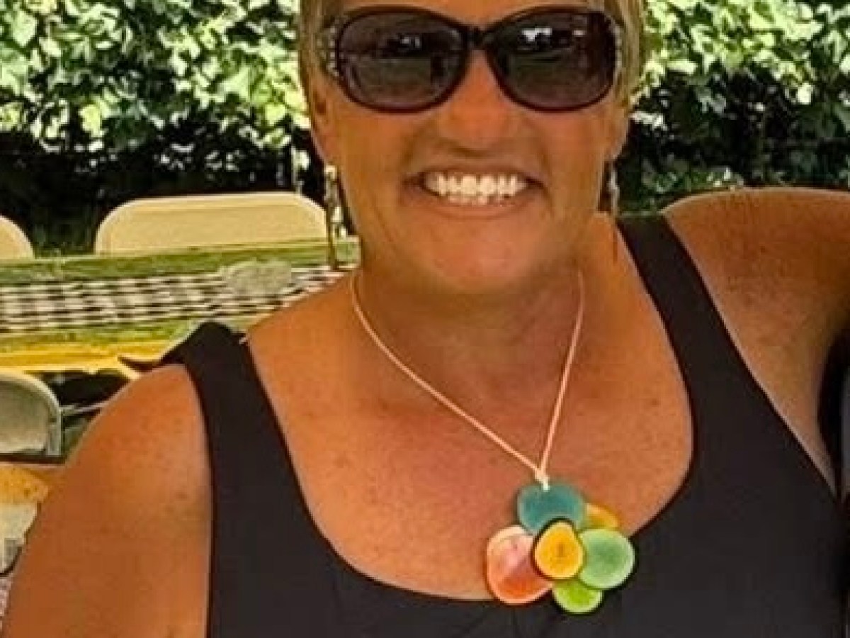 Smiling person with sunglasses, wearing a flower necklace, under a tent.